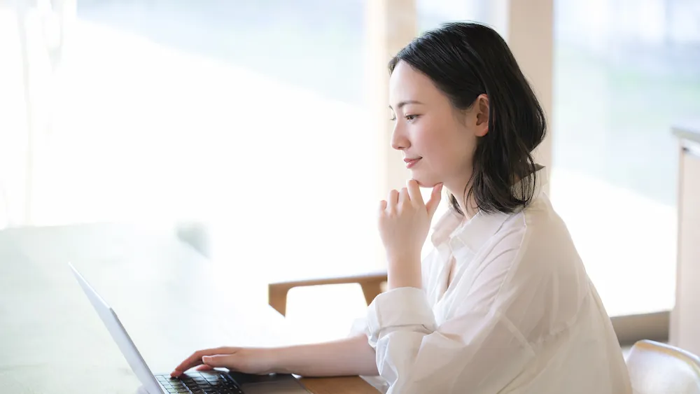 パソコンを見ながら考える女性のイメージ画像
