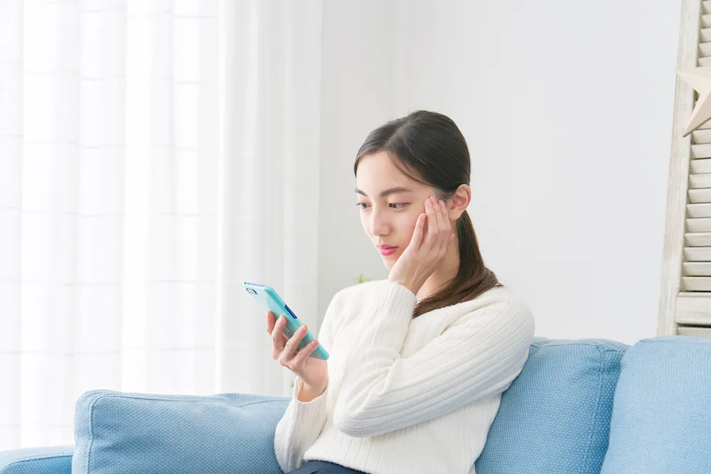 スマートフォンを見て悩む女性の画像