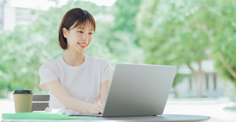 屋外でノートパソコンを操作する女性の画像
