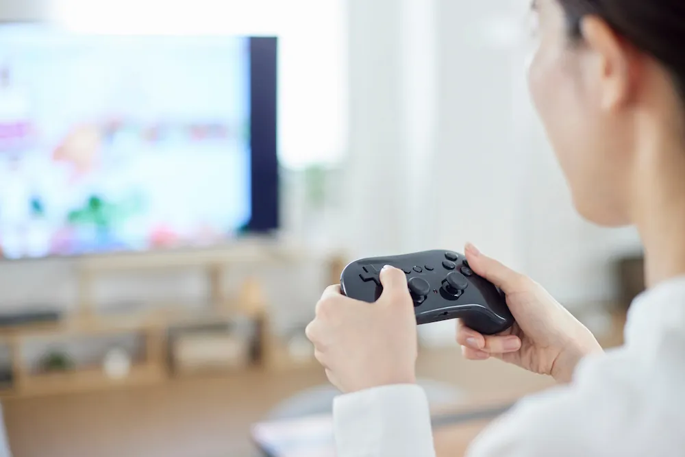 コントローラーを使ってテレビゲームをプレイする女性のイメージ画像