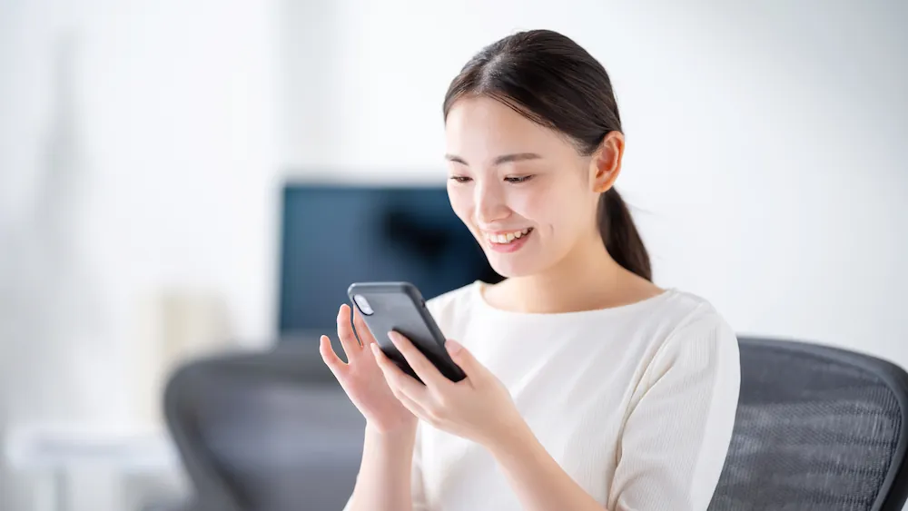 自宅でスマートフォンを操作する女性のイメージ画像