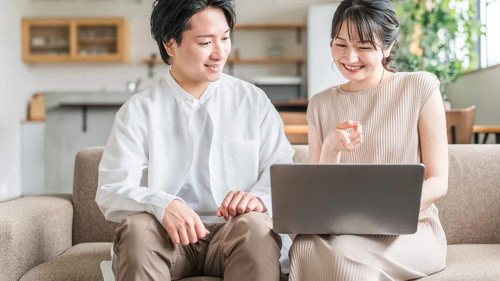 ソファに座ってパソコンを操作する夫婦のイメージ画像